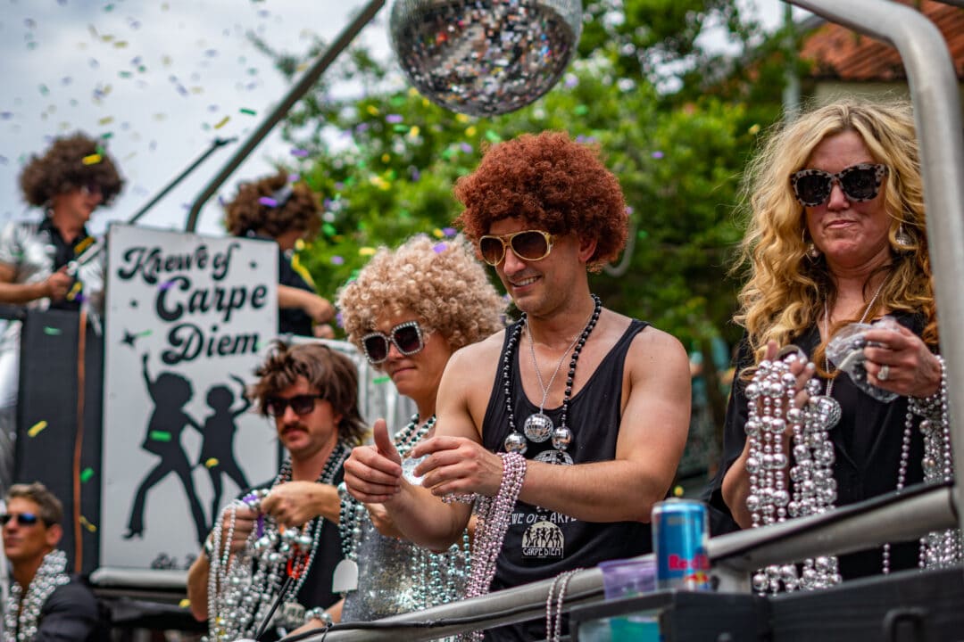 People in zany wigs stand atop a Mardi Gras float in Pensacola, Florida, waiting to toss beads to onlookers.