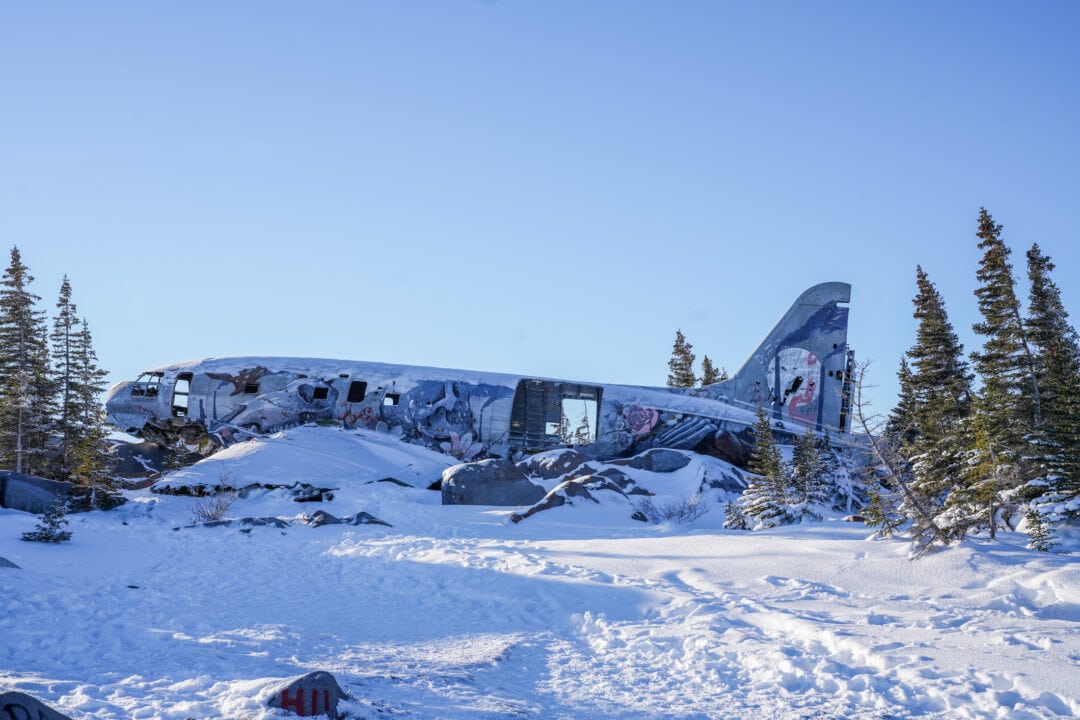 A deserted cargo plane sits in ruin in the middle of a snowy field.