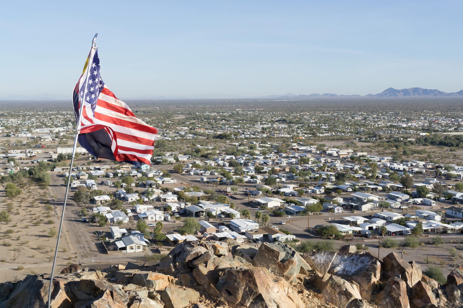 An American flag flies on a hilltop overlooking an RV park.