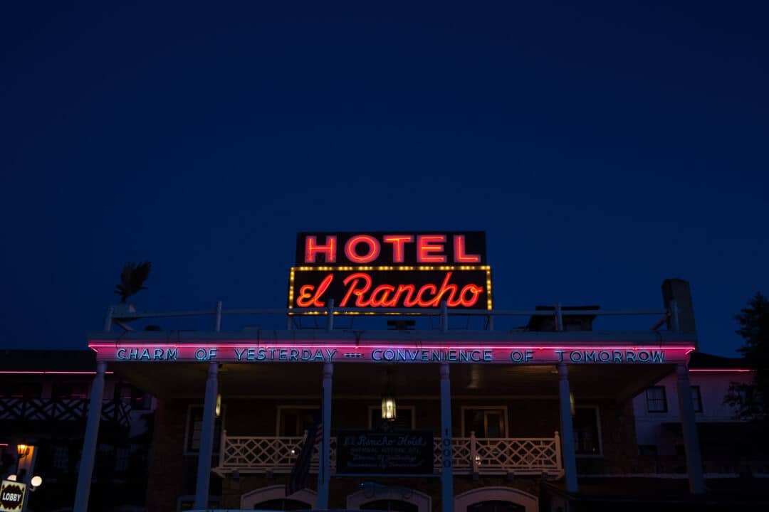 the front of the hotel el rancho at night, with blue, red and pink neon signs lit up against the dark sky