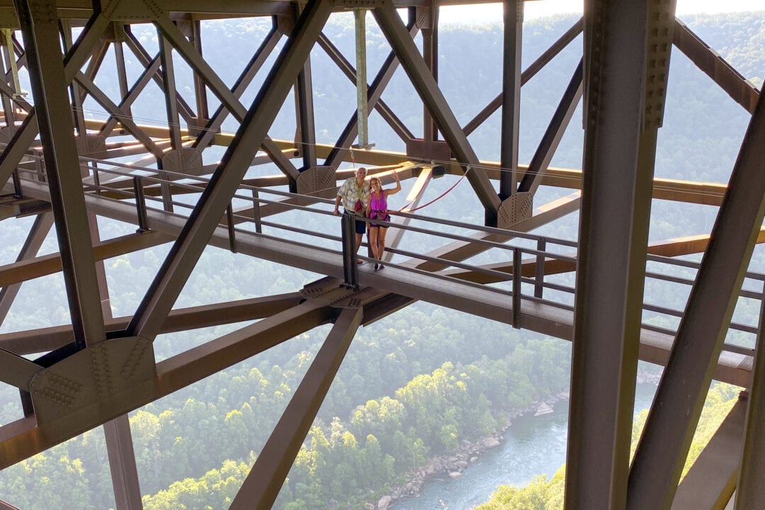 High above a West Virginia gorge two adventurers wave from atop a bridge