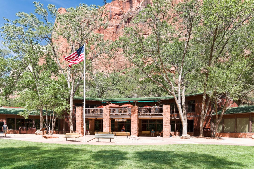 National park lodge on a sunny day with towering red rock behind it