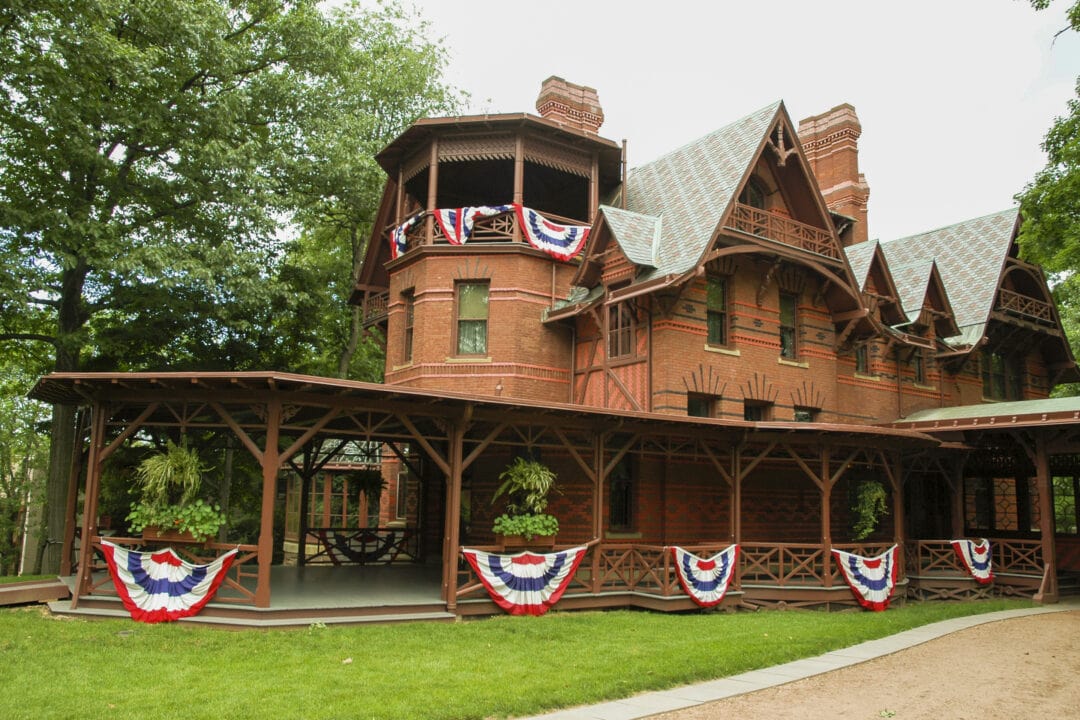 a gothic brick house with a long porch draped in red white and blue bunting