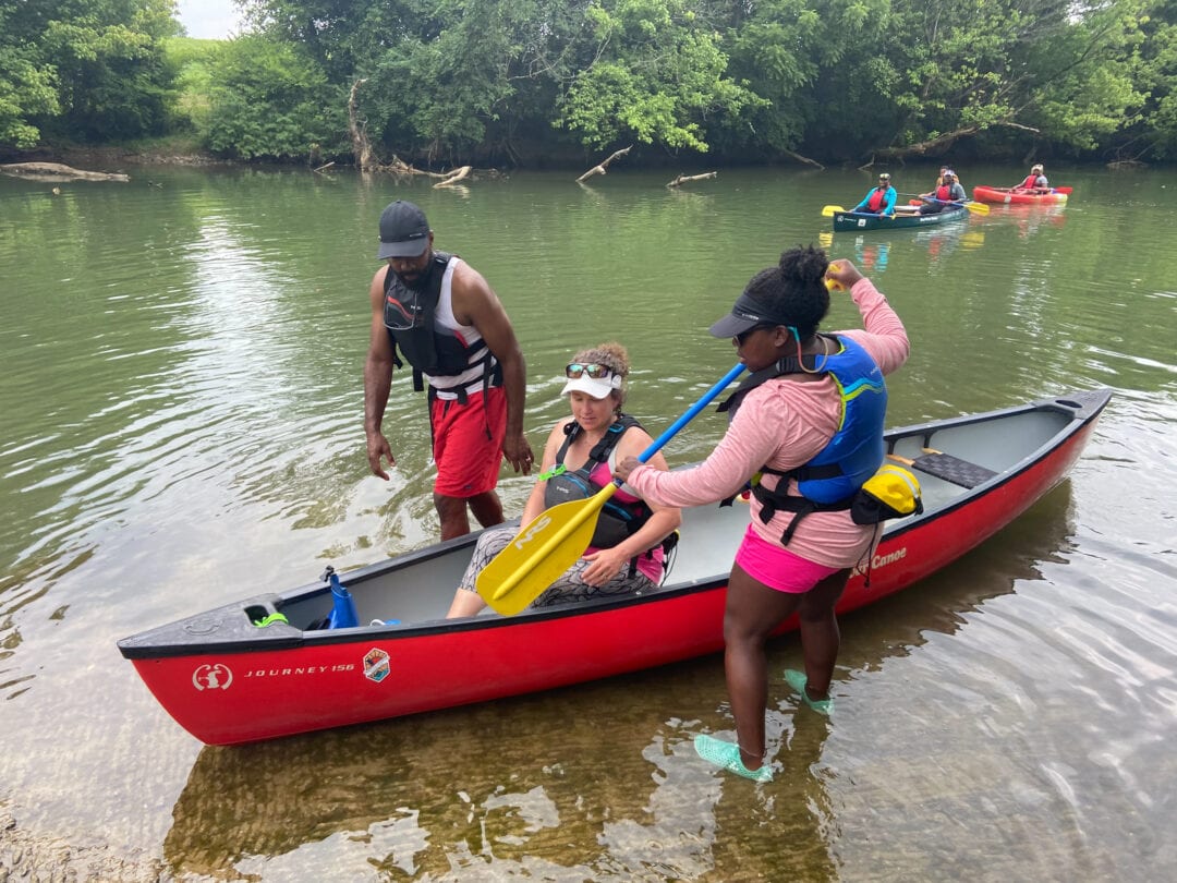 Two people help a woman seated in a red kayak