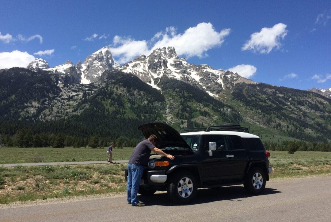 Person checking under the hood a vehicle in scenic locaiton