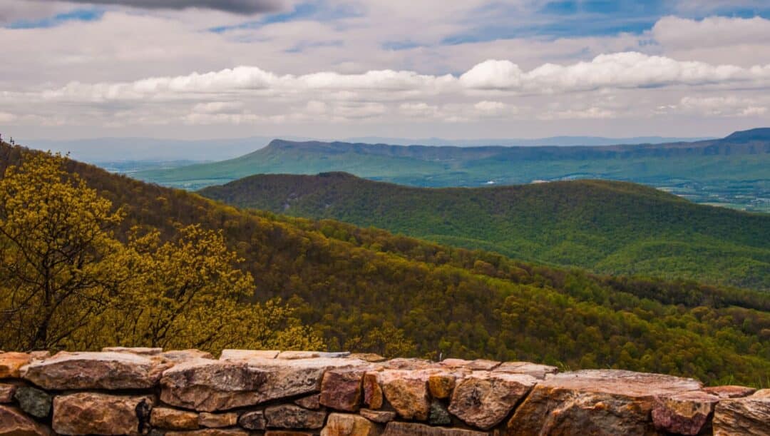 a rock wall and a scenic lush green overlook under cloudy skies